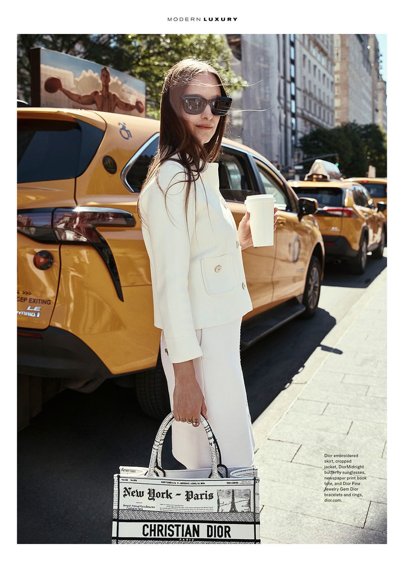 Editorial fashion shot in New York City featuring an adult female model in a white suit, sunglasses, and Dior tote, beside a yellow taxi.