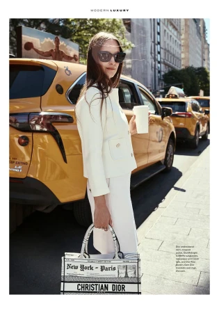 Editorial fashion shot in New York City featuring an adult female model in a white suit, sunglasses, and Dior tote, beside a yellow taxi.