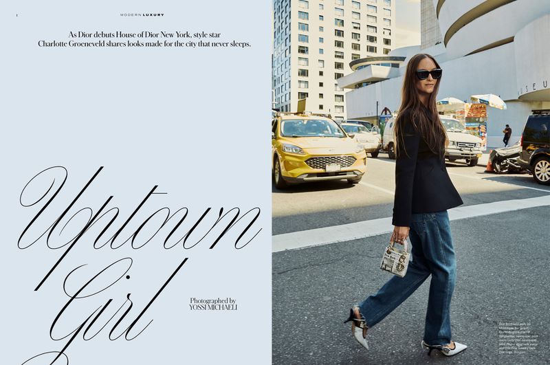 Stylish adult woman walks on a city street wearing a blazer, jeans, and sunglasses, carrying a small purse with a taxi and buildings.