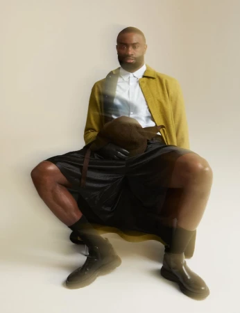 Jaylen Brown seated wearing a yellow jacket, white shirt, and black shorts against an off-white studio backdrop.