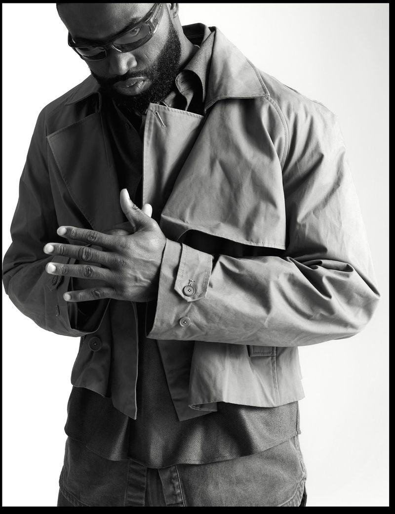 Black and white portrait of Jaylen Brown wearing sunglasses and a cropped trench jacket against a white studio background.
