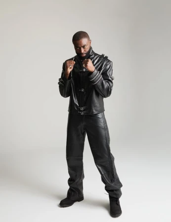 Jaylen Brown posing in a boxing stance wearing a black leather buckled jacket and black leather pants against a studio backdrop.