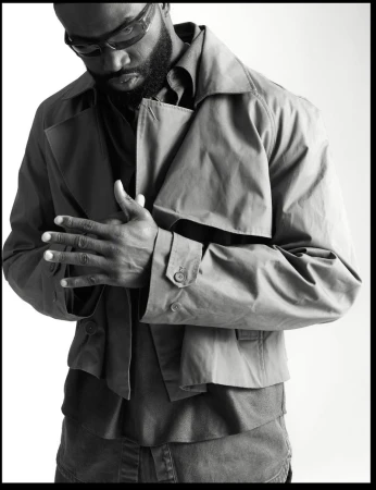 Black and white portrait of Jaylen Brown wearing sunglasses and a cropped trench jacket against a white studio background.