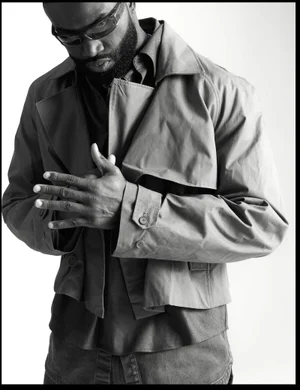 Black and white portrait of Jaylen Brown wearing sunglasses and a cropped trench jacket against a white studio background.