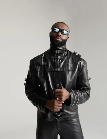 Jaylen Brown wearing a black buckled leather jacket and futuristic sunglasses against a light grey seamless backdrop.