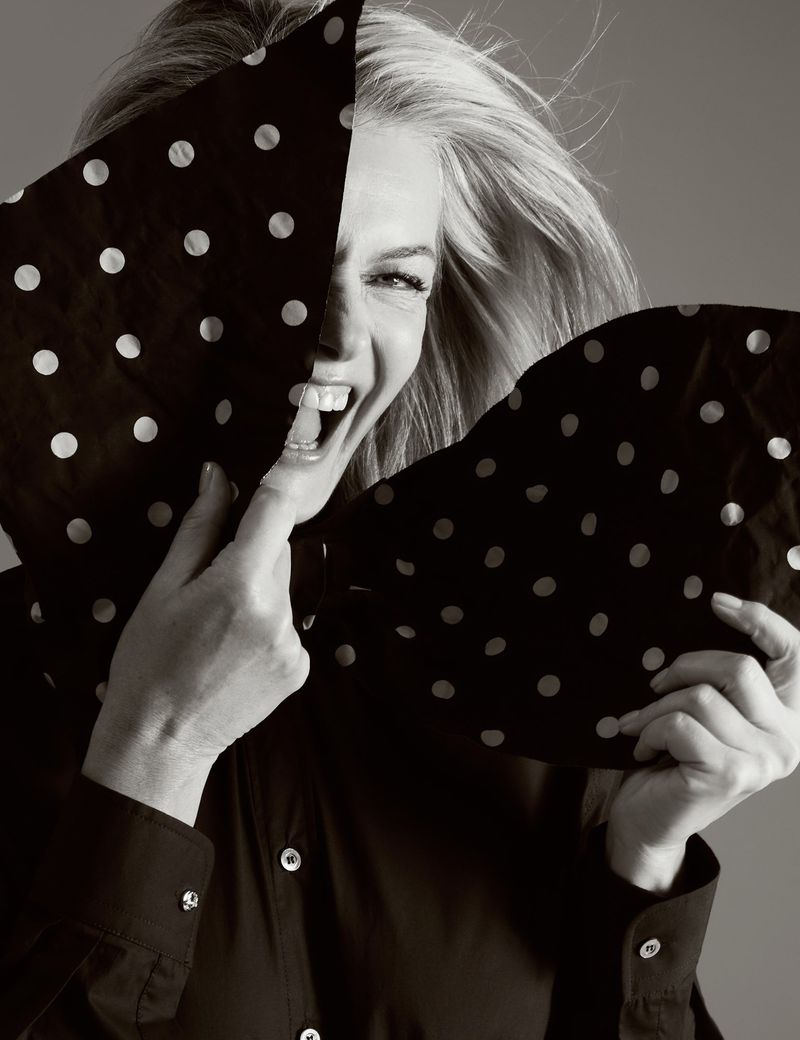 Monochrome portrait of an adult woman laughing, partly obscured by a polka-dot textile held up in front of her face.