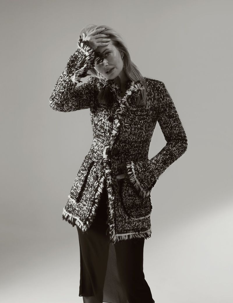 Monochrome portrait of a blonde adult female model in a textured jacket, striking a pose in a photo studio with neutral backdrop.