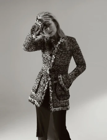 Monochrome portrait of a blonde adult female model in a textured jacket, striking a pose in a photo studio with neutral backdrop.