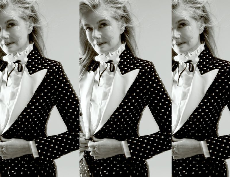 Older woman poses in polka dot blazer and white blouse against light background. Black-and-white fashion portrait.