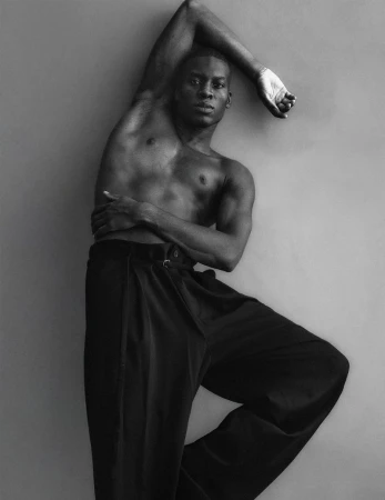 Portrait of an African American man with bare chest wearing black pants in a fashion pose against a grey background in black and white.