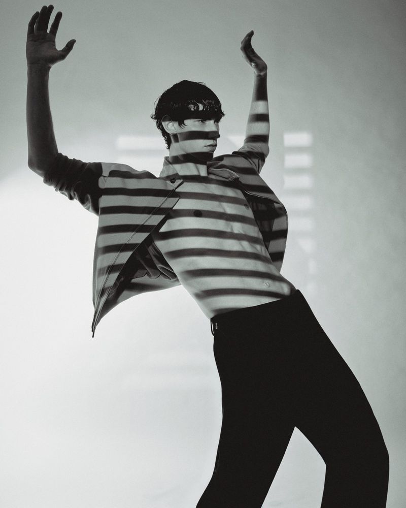 Artistic monochrome portrait of a slender adult male posing with arms raised, covered with a horizontal striped pattern, minimalist studio.