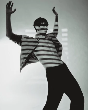 Artistic monochrome portrait of a slender adult male posing with arms raised, covered with a horizontal striped pattern, minimalist studio.