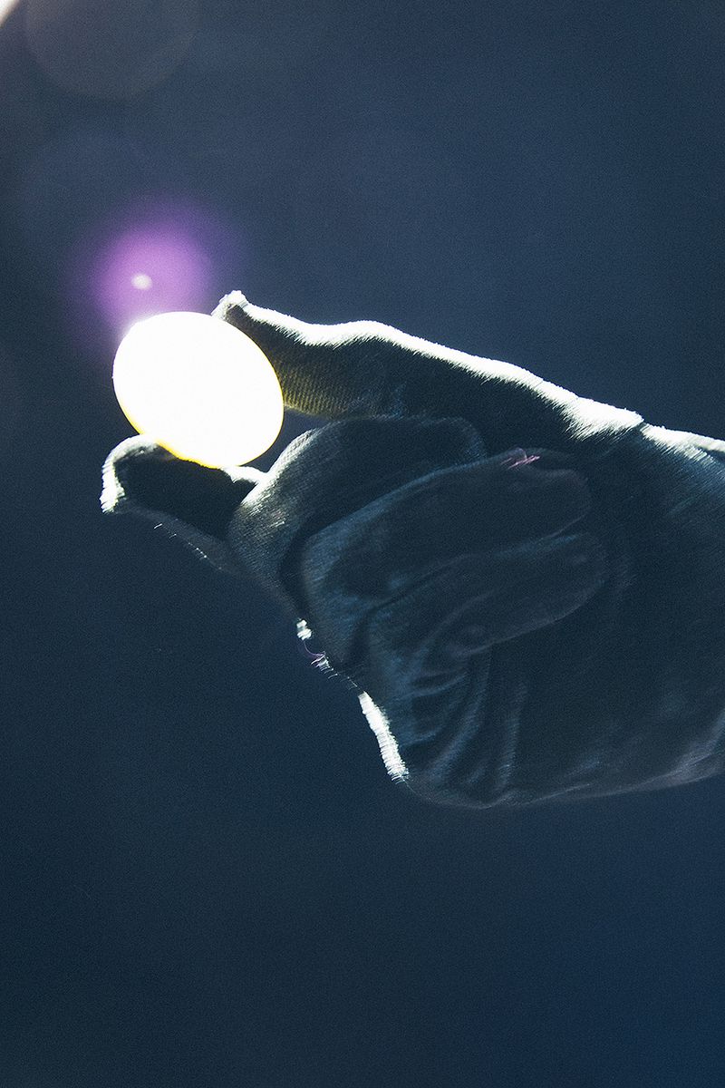A gloved hand holds a luminous, glowing ball against a dark backdrop, creating a striking contrast and focus on the object.