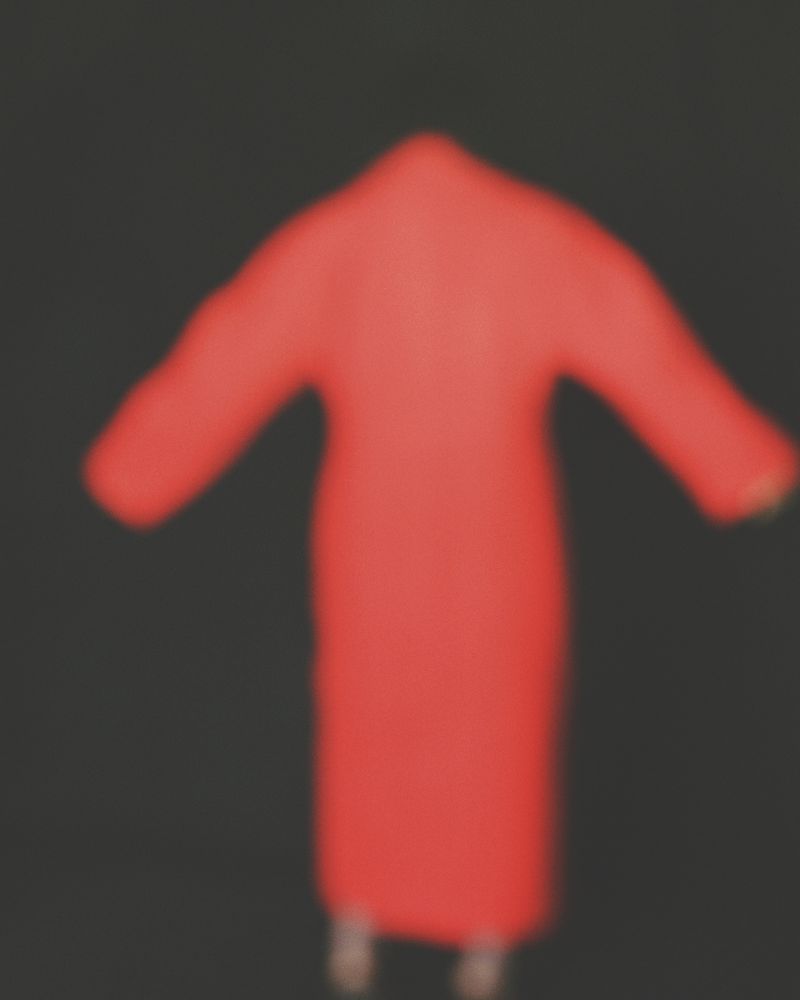 Blurred view of a person wearing a red robe, creating a hazy and indistinct image with a dark background.