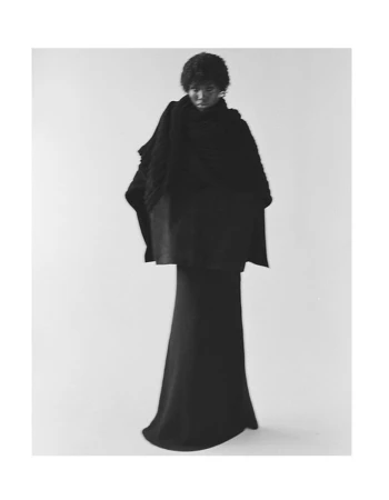 Model wearing a black oversized shawl and long skirt standing against a plain white studio backdrop