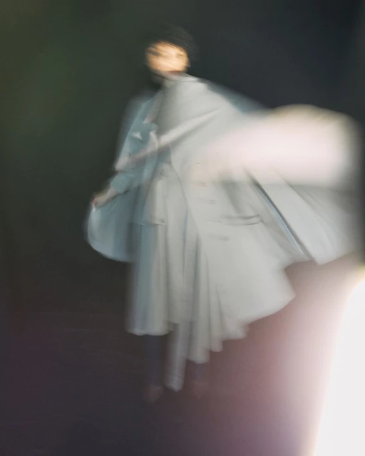 Ghostly blurred motion portrait of a woman wearing light-blue coat on black background with soft focus and shallow depth of field.