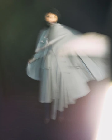 Ghostly blurred motion portrait of a woman wearing light-blue coat on black background with soft focus and shallow depth of field.