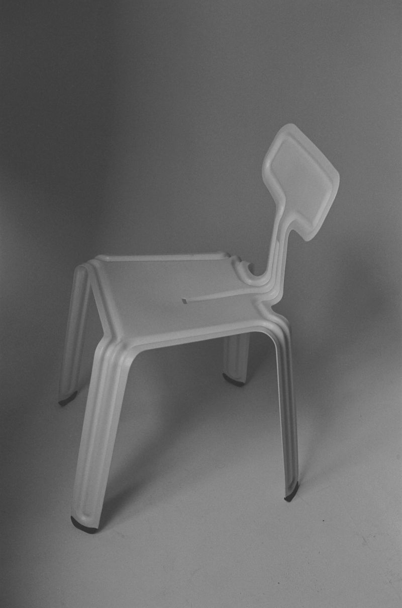 Monochromatic shot of a translucent white plastic chair with a backrest on a light grey seamless background in a minimalist studio setting.