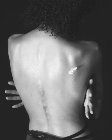 Black and white portrait focusing on the bare back of a person with a single white feather resting against the shoulder blade.