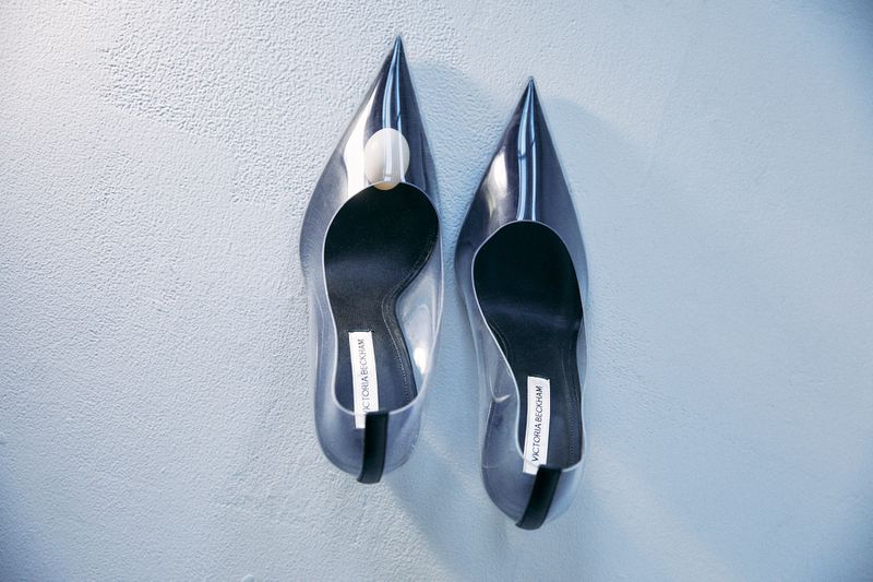 Elevated view of clear stiletto heels with pointed toes and a designer label set against a textured off-white background.