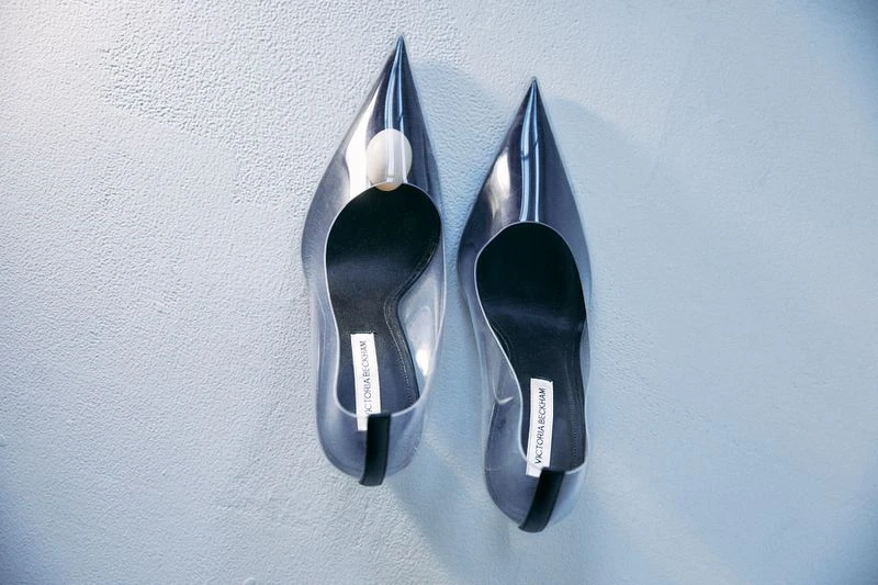 Elevated view of clear stiletto heels with pointed toes and a designer label set against a textured off-white background.