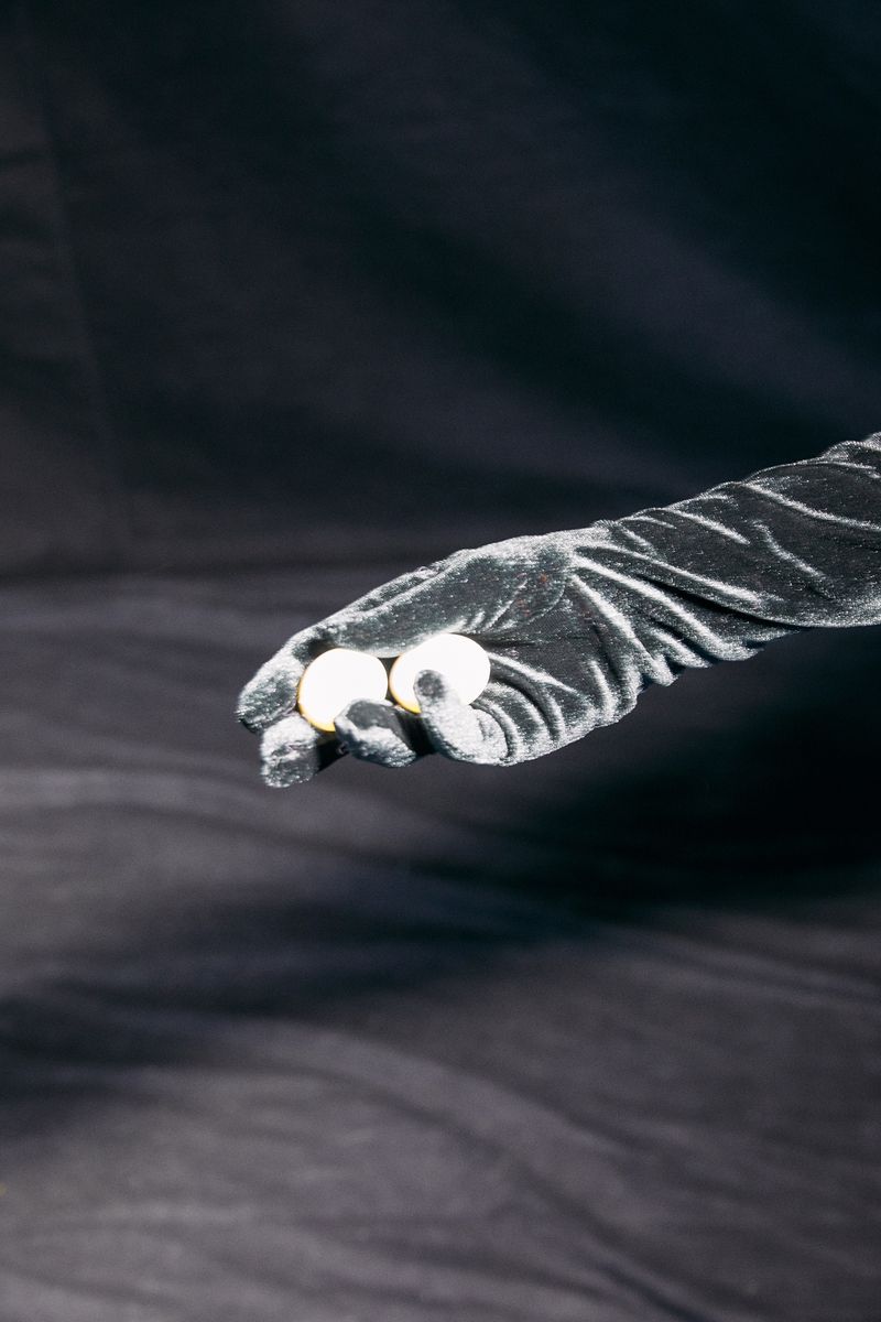 Close-up of a hand in a black glove holding two white balls against a blurred dark background, showcasing textures and contrasting tones.