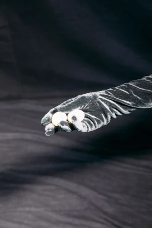 Close-up of a hand in a black glove holding two white balls against a blurred dark background, showcasing textures and contrasting tones.