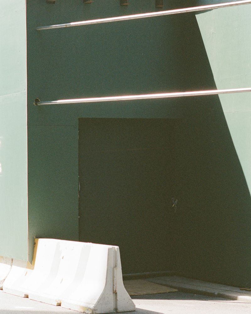 An exterior view shows a green wall with metal bars, a dark door, and a white and gray traffic barrier on the street.