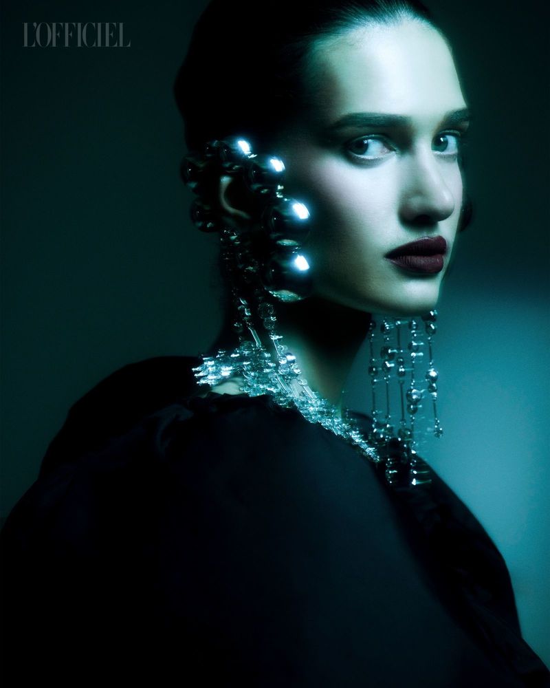 Close-up portrait of a woman with dark hair and deep red lips wearing an elaborate glowing and reflective silver ear cuff earring.
