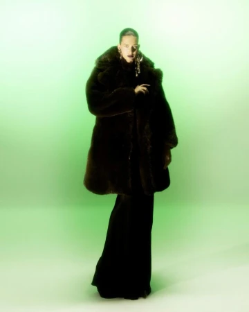 Model in a dark furry coat and long black skirt against a glowing green studio backdrop for L'Officiel India.
