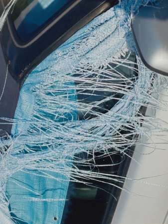 Damaged car windshield with shattered glass and blue tarp. Close-up shot showing the extent of damage to the vehicle's glass.