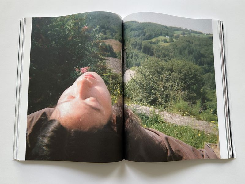 Open book double-page spread featuring a young woman reclining outdoors in nature, with a lush green forest landscape in the background.