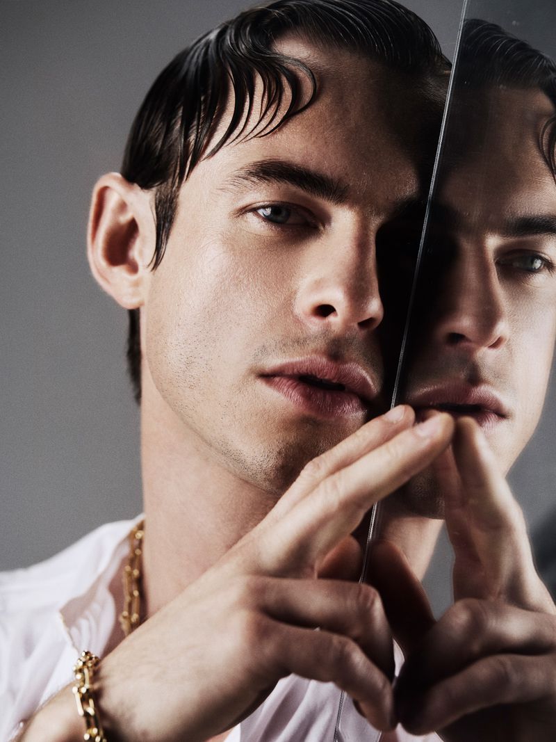 Close-up portrait of a handsome adult male with dark hair styled in retro waves, wearing gold jewelry and a white shirt, studio shot.