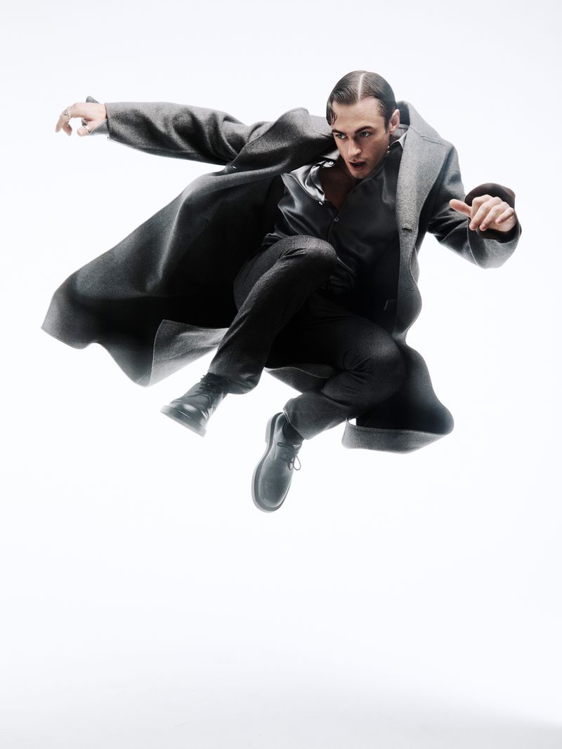 A person in a gray coat mid-air, captured in a dynamic studio shot on a white backdrop, showcasing fashion and movement in a single frame.