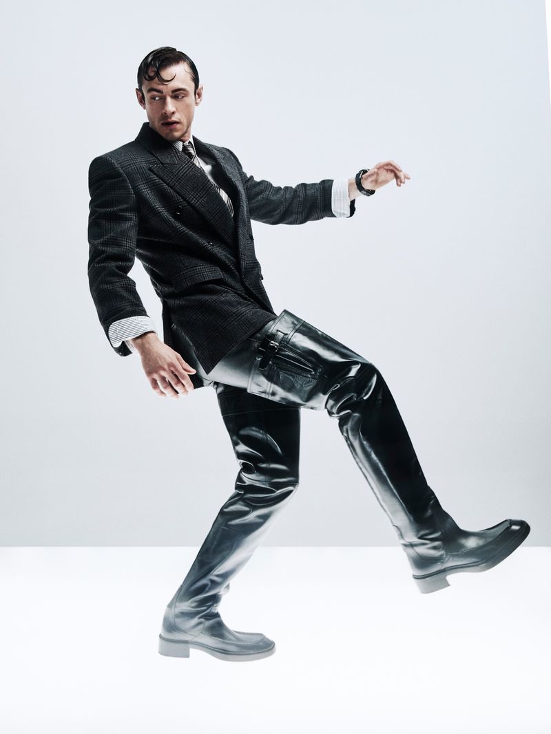 Fashion photo of a man in a suit and tall black boots posing in a studio. Dramatic lighting highlights textures of fabric and leather.