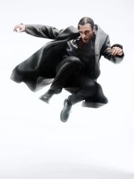 Man wearing a long grey coat leaping through the air against a bright white background