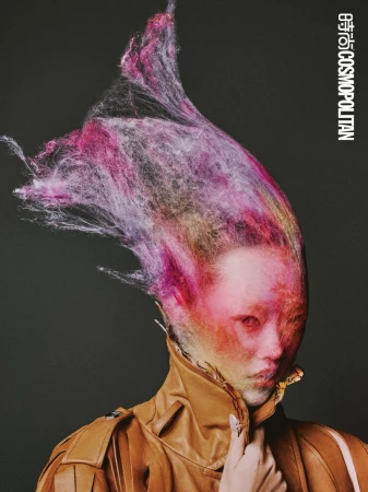 Portrait of a person with theatrical makeup and a tan jacket. The subject's hair is an explosion of multicolored, fiber-like strands.