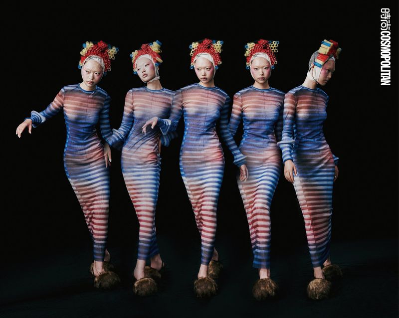 Five Asian women in striped dresses and elaborate headwear pose in a studio against a black background for a fashion editorial.