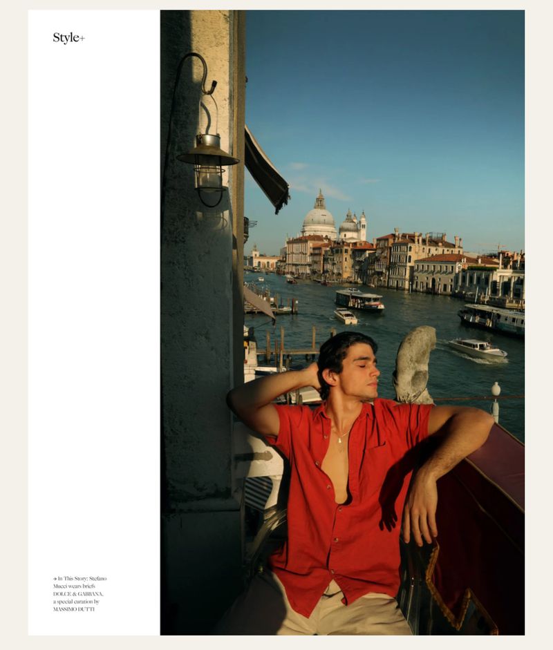 Young man in red shirt on Venice balcony with gondolas, canals, and dome in the background on a bright day. Editorial fashion shot.