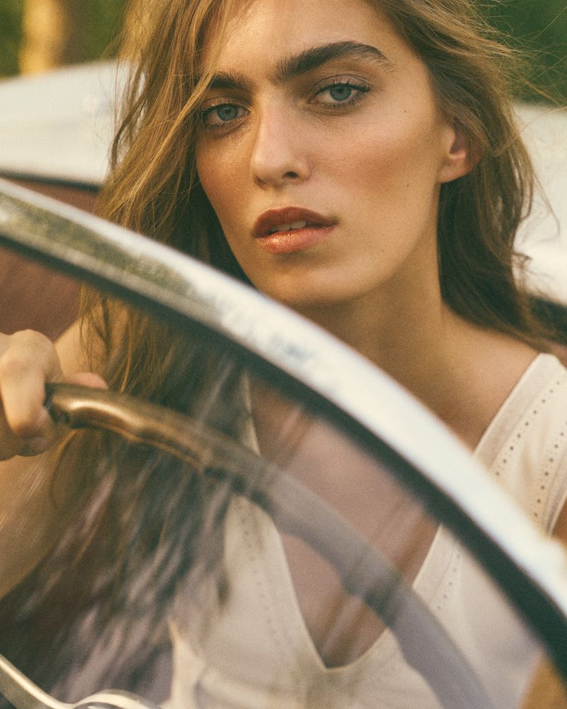 Close-up of a woman with long hair in a car, showcasing a natural beauty style with focus on face, hair, and vehicle interior.