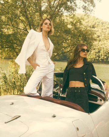 Two female models posing with a vintage white convertible car in an outdoor landscape setting for Schön! Switzerland