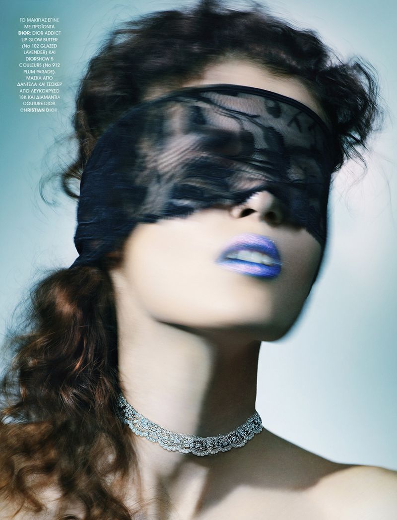 Fashion shot of woman with black lace blindfold, blue lipstick and jeweled choker, soft lighting and muted blue background.