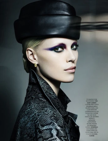 Fashion editorial portrait of a fair-skinned adult woman wearing a black hat and a snakeskin jacket against a neutral background.