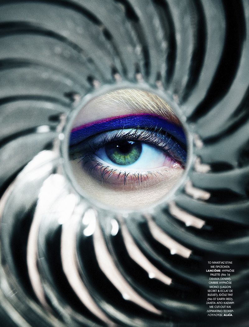 Close-up studio shot of a woman's eye with vibrant purple and pink makeup, set against a silver, radial background and soft studio lighting.