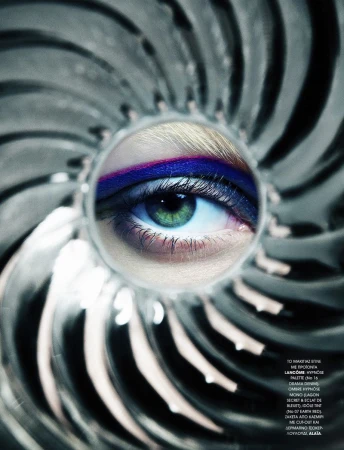 Close-up studio shot of a woman's eye with vibrant purple and pink makeup, set against a silver, radial background and soft studio lighting.