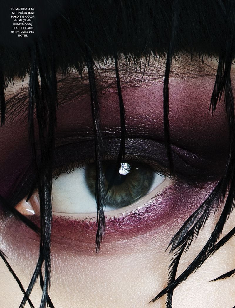 Close-up of a woman's eye with dramatic purple eyeshadow and prominent black feathered headpiece, showcasing beauty and fashion details.
