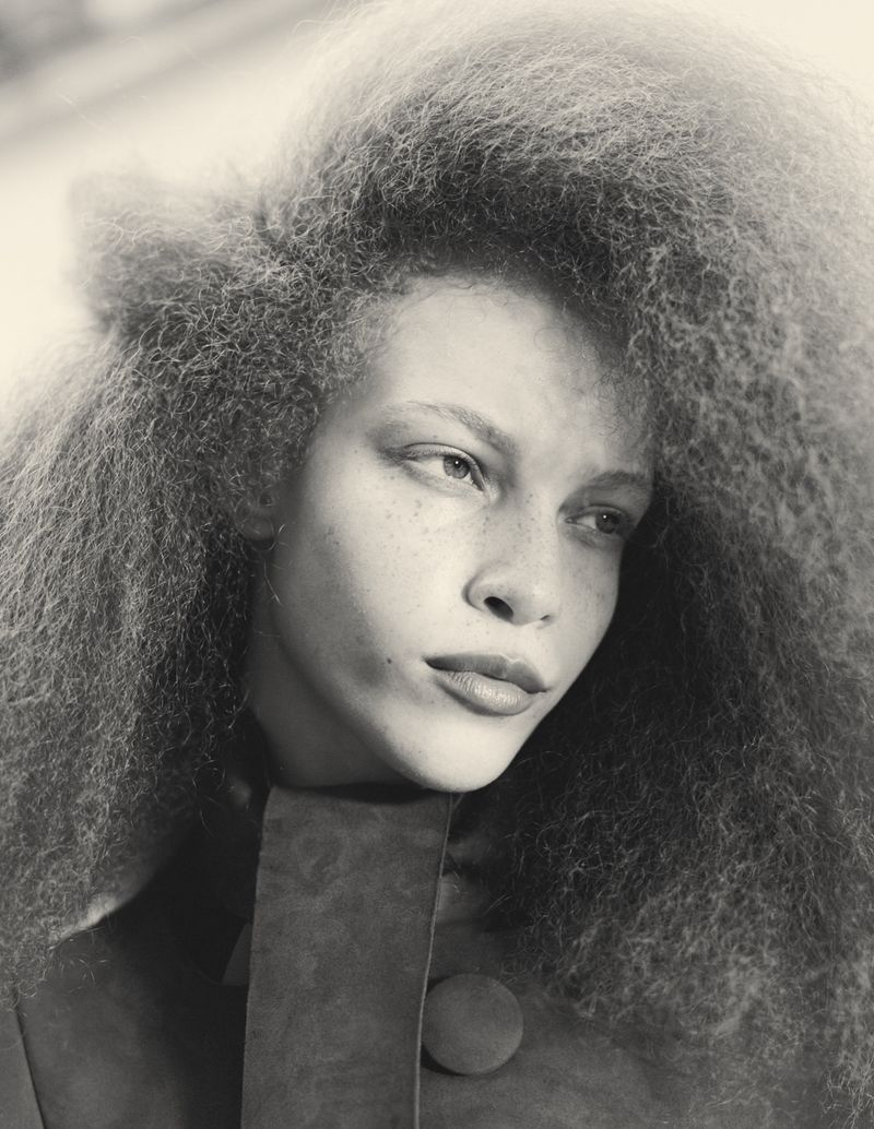 Monochrome portrait of a model with freckles and curly hair, wearing a textured top with a button, captured in a studio setting.
