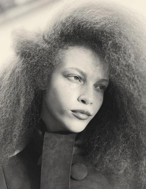 Monochrome portrait of a model with freckles and curly hair, wearing a textured top with a button, captured in a studio setting.