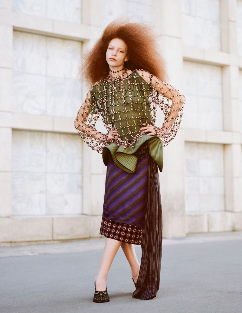 Fashionable adult female model with a large afro hairstyle wearing a green top and skirt posing in front of a building outdoors.