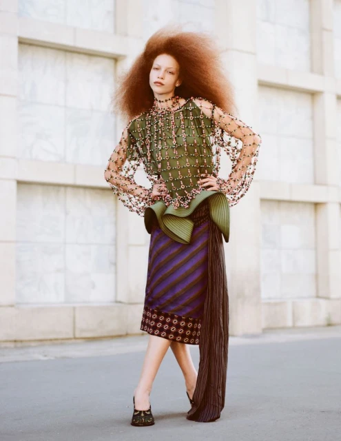 Fashionable adult female model with a large afro hairstyle wearing a green top and skirt posing in front of a building outdoors.